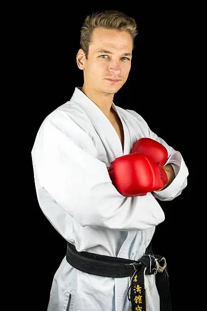 Young professional kick box fighter looking confident and satisfied. Isolated over black background.