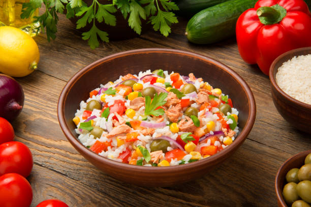 Tuna and rice salad in a terracotta salad bowl on a rustic wooden table with ingredients. stock photo