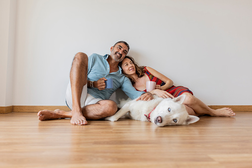 mature couple relaxing at home sitting on the floor with their dog and drinking coffee