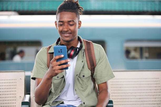 istock Young Man Commuting To Work On Train Sitting  On Platform Looking At Mobile Phone For Travel Information Or Social Media 1850391718