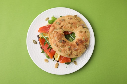 Tasty bagel with salmon and tomatoes on light green background, top view