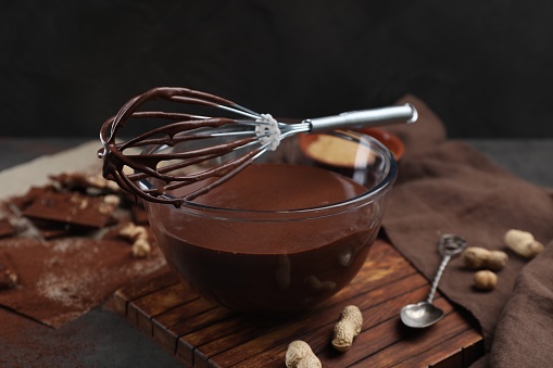 Bowl of chocolate cream and whisk on table, closeup