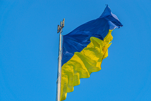 Emblem of Ukraine. Ukraine flag large national symbol fluttering in blue sky. Large yellow blue Ukrainian state flag. National flag of Ukraine against blue sky. Detail of the national flag of Ukraine. Emblem of Ukraine