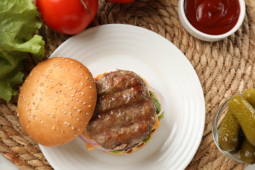 Hamburger with lettuce, onions, tomato, and pickle open face on a sesame bun.  All on a white plate.  Isolated with a clipping path.