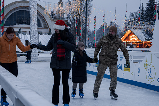 Kyiv, Ukraine - December 12, 2023: People came to the New Year fair to relax after a working day and go ice skating. parents with children walk and drink hot drinks to warm up in cold weather.