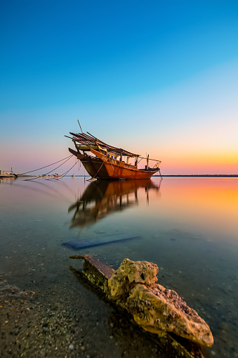 Golden hues paint the tranquil Dammam seaside as boats rest against the morning glow, a serene embrace of nature's beauty in Saudi Arabia.