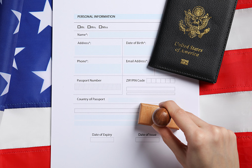 Immigration to USA. Woman stamping visa application form on flag, top view