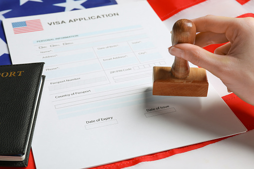 Immigration to USA. Woman stamping visa application form on flag, closeup
