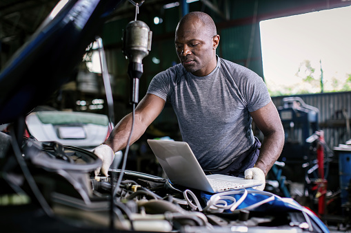 Mechanic using compute for Diagnostic  machine tools ready to be used with car. Car mechanic using a computer laptop to diagnosing and check up on car engines parts for fixing and repair