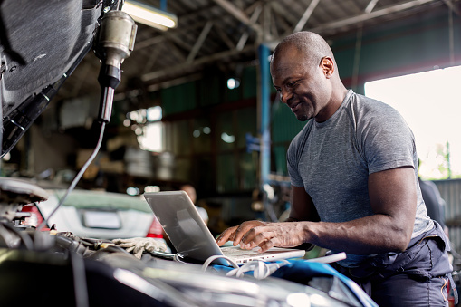 Mechanic using compute for Diagnostic  machine tools ready to be used with car. Car mechanic using a computer laptop to diagnosing and check up on car engines parts for fixing and repair