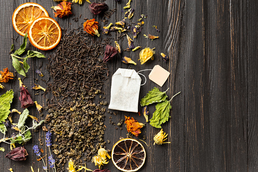 Composition of dry black and green tea, tea bag, dried citrus slices and dry hibiscus flowers on a dark wooden background top view. Different types of dry tea on a dark background.