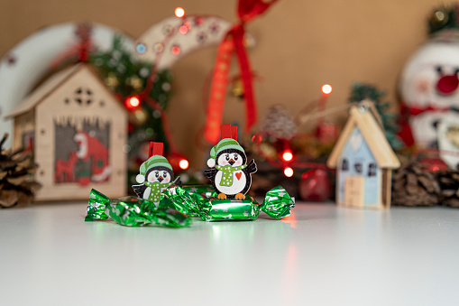 Two penguin Christmas decorations standing on Christmas candy with decorations behind, small red lights