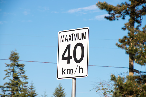 Sign limiting the speed of movement to 30 miles per hour of measurement on a street lighting pole, close-up shooting from a distance and with the perspective of the roofs of houses in blue sky.