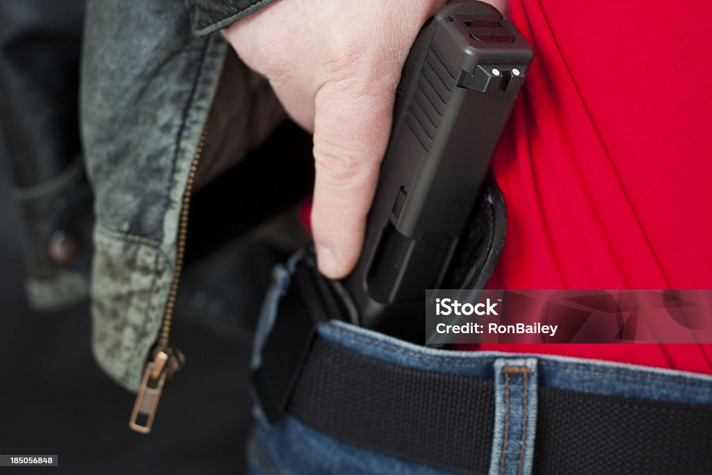 Concealed Carry Firearm Drawn From an Inside-the-Waistband Holster A caucasian man drawing his modern polymer (Glock) .45 caliber pistol from an IWB (inside the waistband) holster under his leather jacket.  Showing proper trigger control by keeping his finger off the trigger as he draws.All images in this series... Carrying Stock Photo