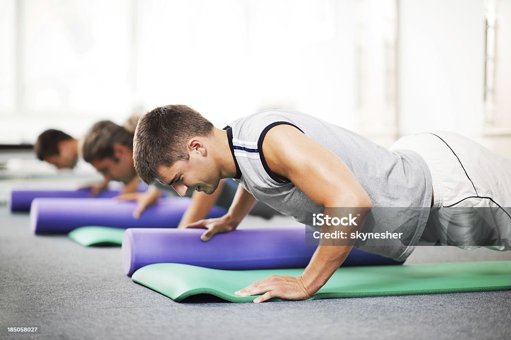 Group of young people doing Pilates exercises. Group of people men exercises on the exercising mat.  They are doing pushups with Pilates rollers.     Gym Stock Photo
