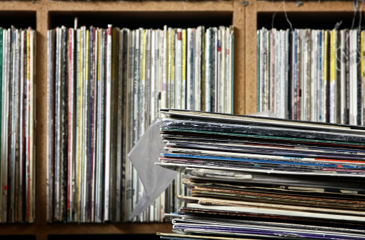 An old stack of records sits in front of a shelf full of vinyl in a local record store.