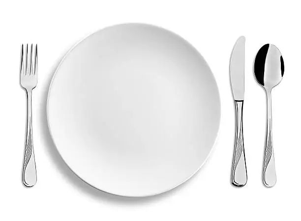 Four clipping paths included. Empty dinner or lunch plate with stainless steel cutlery isolated on white background, studio shot.