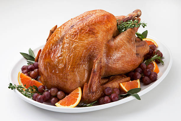 Roast Turkey and Trimmings on a Light Background. Roast turkey on a white oval platter on a white background. The golden brown turkey is garnished with red grape clusters and orange wedges. Sprigs of fresh herbs; thyme, sage and rosemary bring green accents to the colorful presentation. turkey thanksgiving dinner cooked stock pictures, royalty-free photos & images