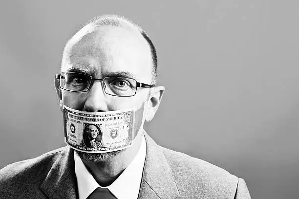 "This balding, slightly nerdy businessman looks unhappy and nervous in his US one dollar bill gag. Black and white shot with plenty of copy space"