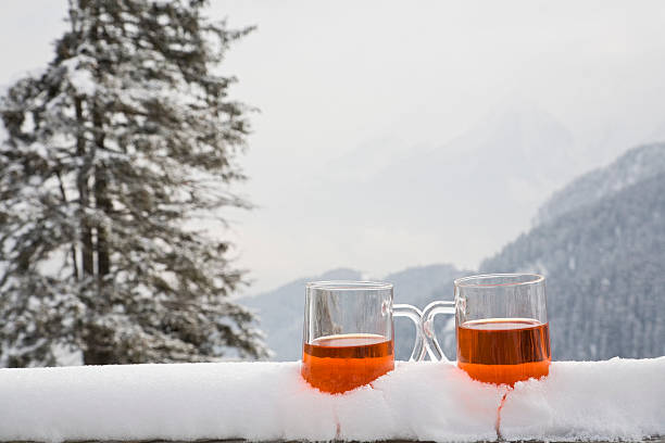 Two glasses of drink sit on a snow covered ledge  two glasses with a hot drink stand in the snow,  apres ski stock pictures, royalty-free photos & images