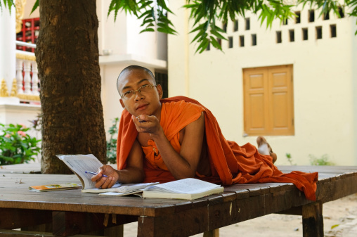 A Burmese Buddhist young man studying in the shade of a tree at his monastery in Mandalay, Myanmar. Many young monks and novices get their education at the monastery.