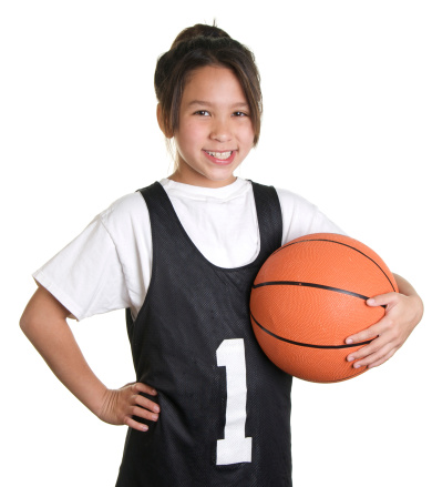 An adorable nine year old girl with a basketball uniform and basketball on a white background.