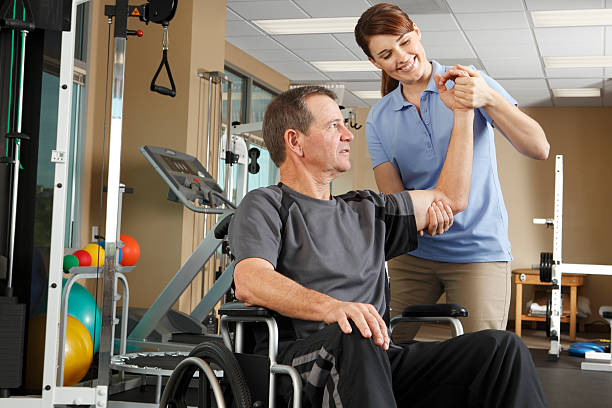 Physical therapist evaluating range of motion of patient in wheelchair A female physical therapist evaluating the range of motion of a  male patient's shoulder. The patient is sitting in a wheelchair.   The therapist is in her early 30's and the patient is in his mid 50's.  Photographed in a clinical setting with several pieces of exercise equipment in the background. paraplegic stock pictures, royalty-free photos & images