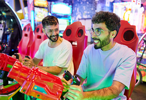 Gay couple having fun in an arcade room. They are playing a game with laser guns. Leisure time.