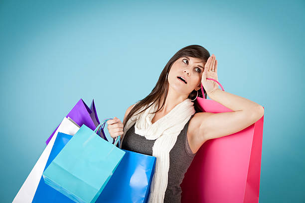 Tired/Frustrated Young Woman with Shopping Bags Color image of a tired/frustrated, young woman carrying all of her shopping bags, with colored background. rolling eyes irritation displeased facial expression stock pictures, royalty-free photos & images