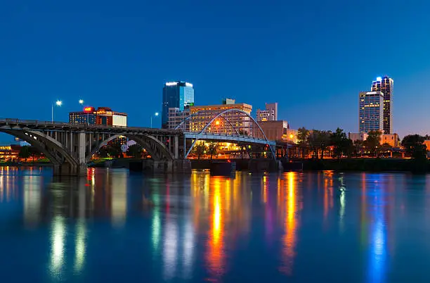 Little Rock downtown skyline with a bridge and the Arkansas River in the foreground at dusk.