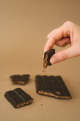 Woman's hands holding a piece of the peanut dark chocolate bar