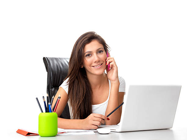 Woman sitting at desk in office and working on laptop while holding mobile phone and talking, new business