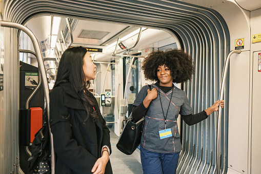 Two female registered nurses riding the street car on the way to work. They are wearing  medical scrubs under winter coats. Urban exterior of busy street in Toronto, Canada.