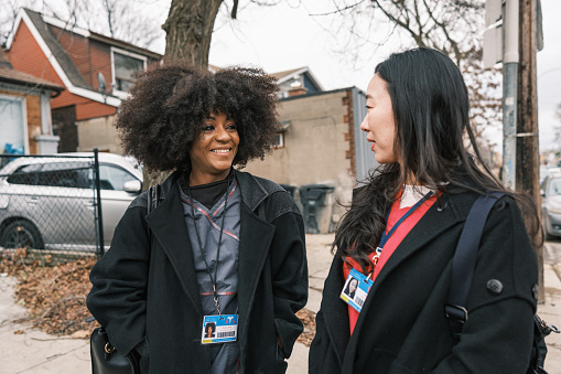 Two female registered nurses on the way to work. They are wearing  medical scrubs under winter coats. Urban exterior of busy street in Toronto, Canada.