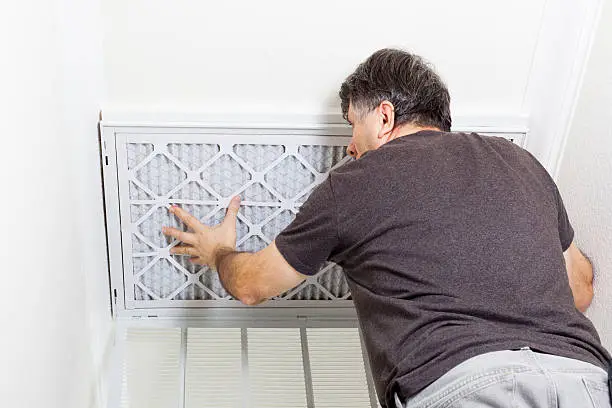 Man replacing a filter on a home air conditioning system.