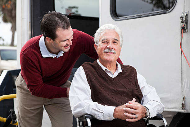 Senior man by minibus with wheelchair lift Young man (20s) helping senior man (60s) in wheelchair, beside shuttle bus equipped with wheelchair lift. wheelchair lift stock pictures, royalty-free photos & images