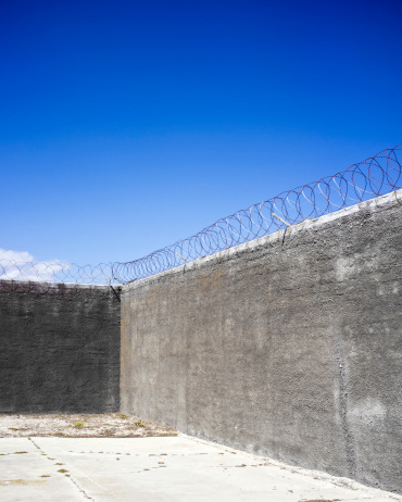 Exterior of a prison with barb wire on top of the wall.