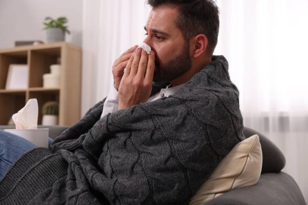 istock Sick man wrapped in blanket with tissue blowing nose on sofa at home. Cold symptoms 1850704653