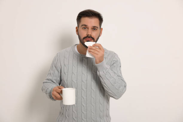 istock Sick man with tissue and cup of drink on light grey background. Cold symptoms 1850707814