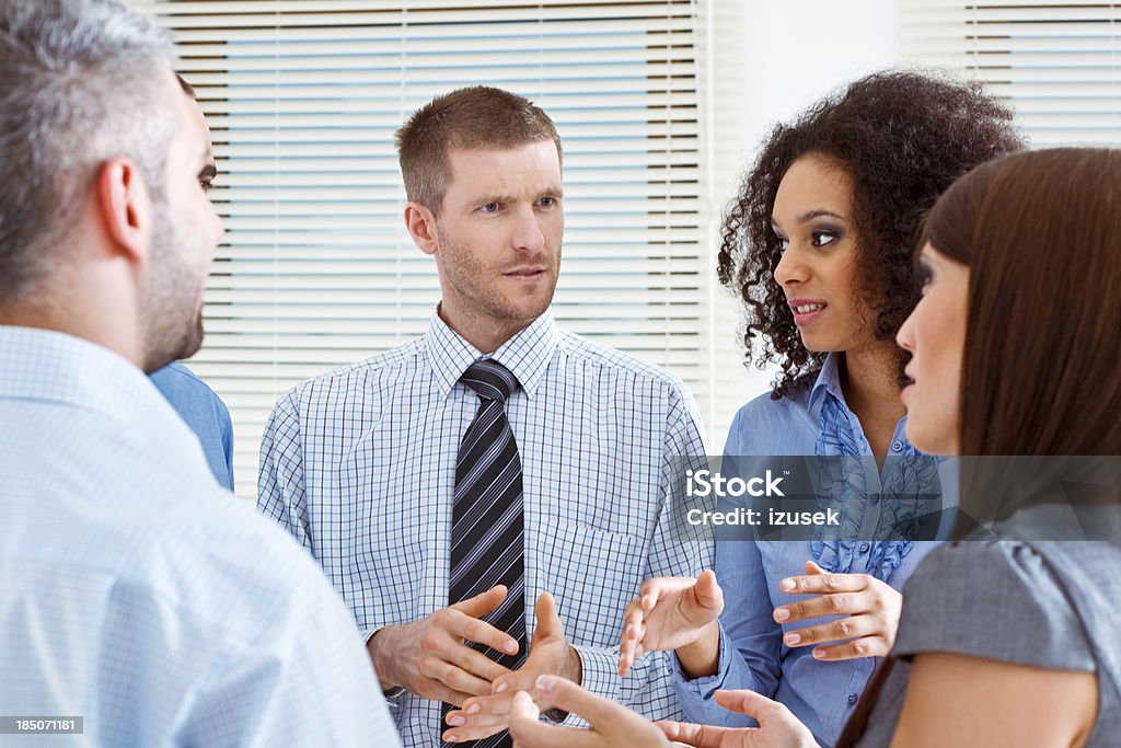 Business Team discussing Group of serious business people standing in an office and talking. 25-29 Years Stock Photo
