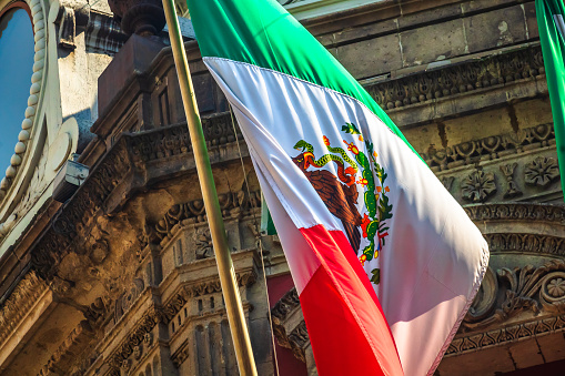 Horizontal view of a Mexican national flag waving in the wind against a clear blue sky.