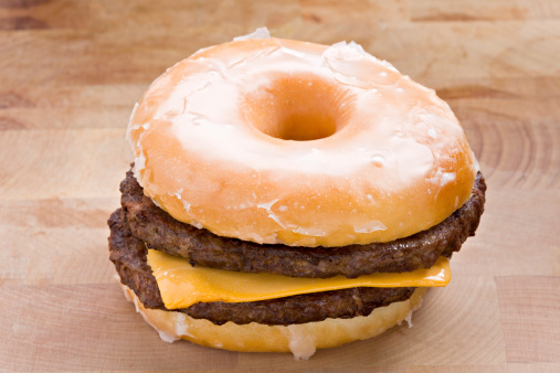 A high angle close up shot of a glazed donut cheeseburger consisting of a slice of american cheese between two grilled sirloin hamburger patties sandwiched between two halves of a glazed donut. Guaranteed to clog your arteries. A concept shot for unusual food cravings and or unhealthy eating.