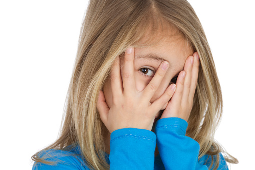 close up of young child hiding behind her hands as a shyness or fear concept
