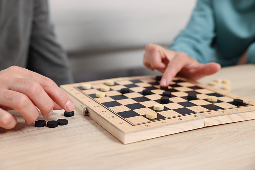 People playing checkers at wooden table, closeup