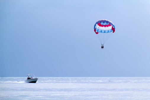 Ayia Napa, Cyprus - June 16, 2018: Parasailing in Agia Napa resort town, motor boat and blue parachute with tourists