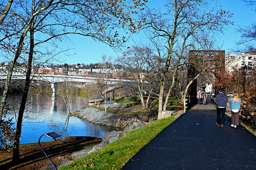 Morgantown, West Virginia, USA - November 25, 2023: A couple walks along the Caperton Trail by the Monongahela River toward a railroad trestle that crosses Deckers Creek on a sunny, cold afternoon.