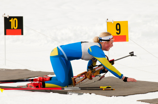 Young female biathlon competitor preparing herself for shooting in lying position