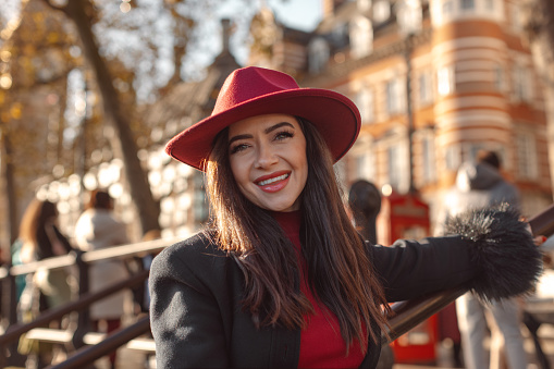Portrait of a stylish and beautiful urban young woman wearing a red hat in London's iconic streets on a sunny day