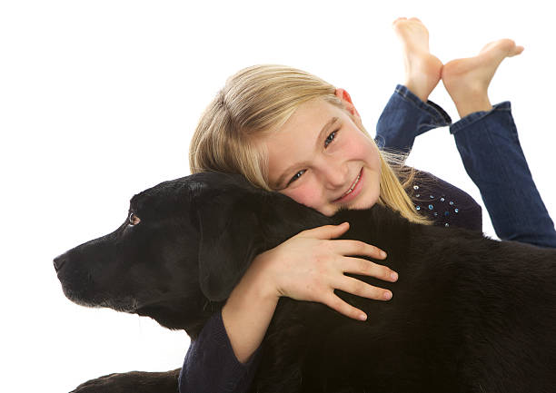 A cute blond girl is hugging her black lab dog.  She's lying down with her barefeet behind her.