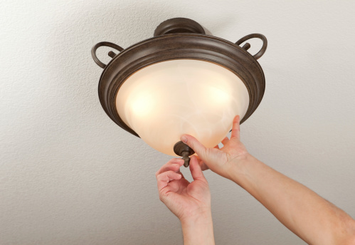 Male hands are installing a glass light fixture dome in a ceiling fixture after replacing light bulbs.